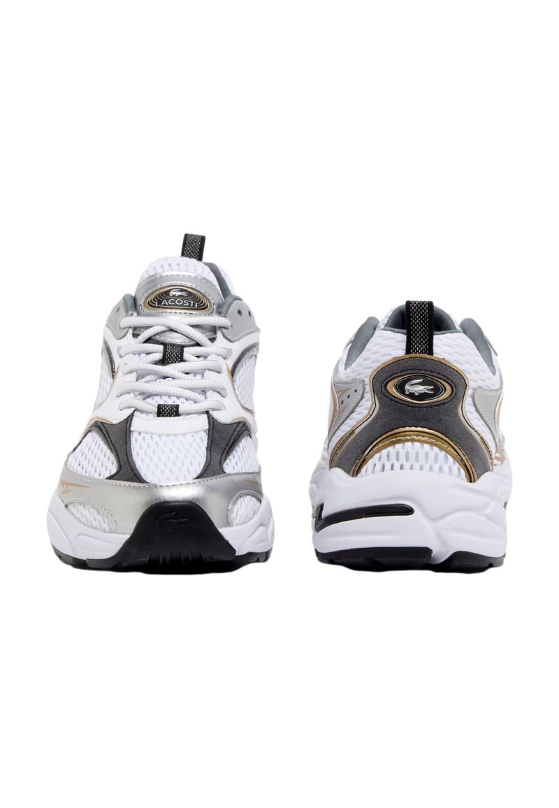 White athletic shoes with grey and silver accents, mesh upper, black outsole, and black laces. Features branding on the tongue and heel.