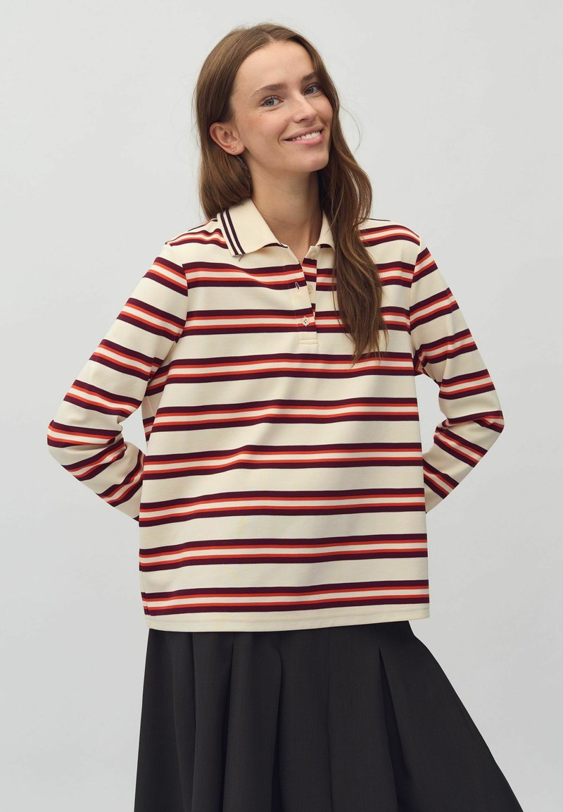 Gestreepte polo in roomkleur, rood en donkerroze. Lange mouwen, knoopsluiting bij de kraag, met een relaxte pasvorm. Gecombineerd met een zwarte geplooide rok.