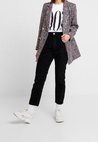 Blazer en tweed avec des fils rouges et bleus, style croisé, associé avec un pantalon en velours côtelé noir et des baskets blanches.