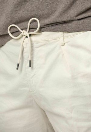 Lichtgekleurde katoenen shorts met een tailleband met trekkoord, met een gladde textuur en een trekkoord met metalen uiteinden. Grijs shirt deels zichtbaar.