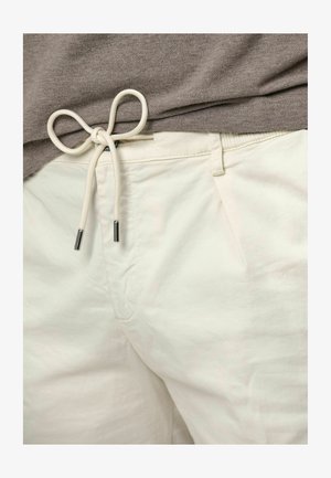 Lichtgekleurde katoenen shorts met een tailleband met trekkoord, met een gladde textuur en een trekkoord met metalen uiteinden. Grijs shirt deels zichtbaar.