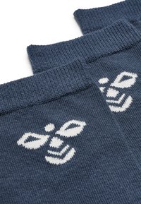 Navyblå strumpor med ribbad struktur som har en vit bi-design stickad vid vristen. Materialet verkar mjukt och elastiskt.