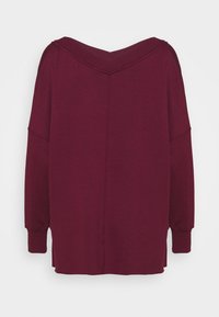 Bordeauxroter Oversize-Pullover mit weitem V-Ausschnitt und angesetzten Schultern. Verfügt über lange Ärmel und Seitenschlitze am Saum für mehr Bewegungsfreiheit.