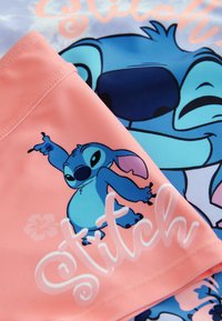 Kaksi kangaspalaa, joilla on Stitch-hahmoja. Toinen on sininen ja vaaleanpunainen printtikuosisena, toinen on yksivärinen vaaleanpunainen valkoisella tekstillä.