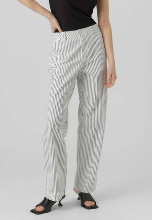 Pantalons rayés en blanc et noir, présentant une taille haute, une coupe droite et une texture de tissu lisse. Accompagnés de chaussures noires à bout ouvert.