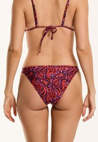 Paisley raksta bikini apakšdaļa ar regulējamiem saitēm aizmugurē, ar spilgtām krāsām, piemēram, sarkanu un purpursarkanu uz tumša fona.