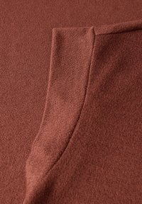 Rustinvärinen neulekangas, jossa on pehmeä rakenne ja sileä, taittuva reuna. Materiaali näyttää kevyeltä ja hengittävältä.