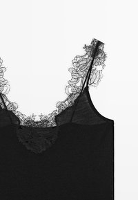 Camisole nero con delicato bordo in pizzo floreale lungo lo scollo e sottili spalline regolabili su sfondo bianco.