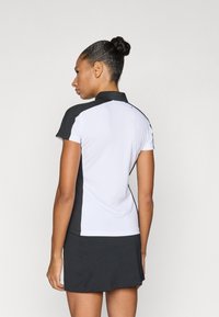 Φόρεμα με κοντά μανίκια, με λευκό πάνω μέρος και μαύρο κάτω, κατασκευασμένο από ύφασμα που απορροφά την υγρασία, με γιακά και υφή σε σημεία του.