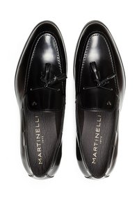 Mocasines de cuero negro con un acabado brillante, que cuentan con un acento de cordón con borlas y una plantilla texturizada, etiquetados como "Martinelli 1973".