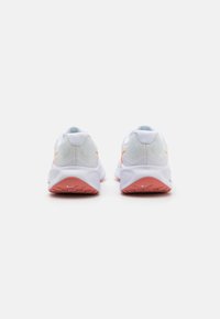 Nike running shoes featuring a white mesh upper, orange accents, and a textured pink rubber sole. Design includes rounded heel and padded collar.