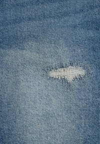 Hellblauer Denimstoff mit einem kleinen horizontalen Riss, der weiße Fäden darunter zeigt und einen abgenutzten Fleck bildet.