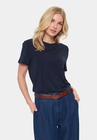 Sötétkék, rövid ujjú póló sima anyagból, magas derekú kék farmernadrággal és barna bőr övvel párosítva.