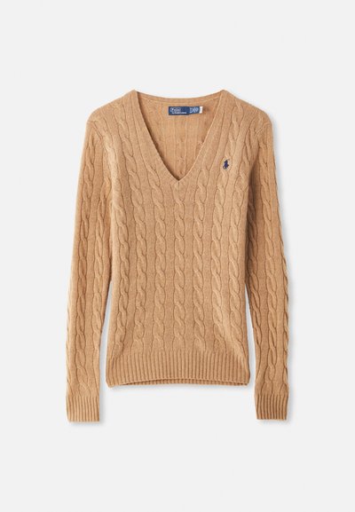 Kamelkrāsas kabelīšu adījuma V-veida kakla džemperis ar garām piedurknēm un mazu tumši zilu izšūtu logo uz krūtīm.