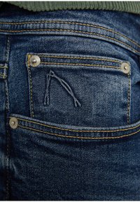 Vaqueros de mezclilla azul con un bolsillo trasero que presenta costuras amarillas y un botón de metal. Textura de la tela visible y un pequeño detalle bordado encima del bolsillo.