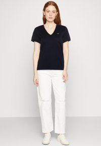 Tricou bleumarin cu decolteu în V, dintr-un material moale, asortat cu pantaloni largi culoarea off-white. Design minimalist, mâneci scurte, fără modele sau accesorii vizibile.