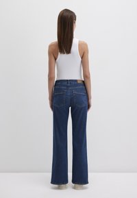 High-waisted, wide-leg denim jeans in dark blue. Features two back pockets and a tan leather patch above the right pocket. Smooth texture.