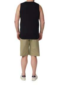 Schwarzes ärmelloses Shirt, lockere Passform, kombiniert mit hellen khakifarbenen Shorts. Die Schuhe sind weiß mit navyblauen und roten Akzenten an der Ferse.