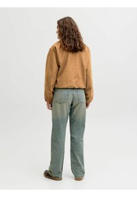 Braunes Wildlederoberteil mit langen Ärmeln in lockerer Passform, kombiniert mit ausgewaschenen blauen Jeans. Die Jeans haben einen lockeren Schnitt und Gesäßtaschen.