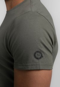 Olivenfarvet kortærmet T-shirt lavet af blødt bomuld, med rund halsudskæring og et lille mørkt logo print på venstre ærme.