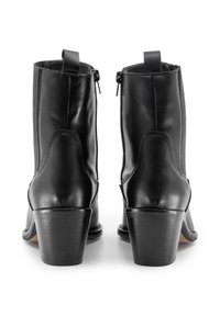 Botas de tobillo de cuero negro con un acabado suave, puntera redondeada y tacón cuadrado. Presentan cremalleras laterales y tiradores para ponerlas fácilmente.