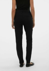 Černé kalhoty sú slim fit, mají hladký povrch, dvě zadní kapsy a střední pas. Nosené s plochými botami.