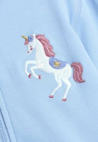 Unicornio blanco con melena rosa, cuerno dorado y silla de montar azul con una estrella bordada en tela azul claro cerca de la cremallera.