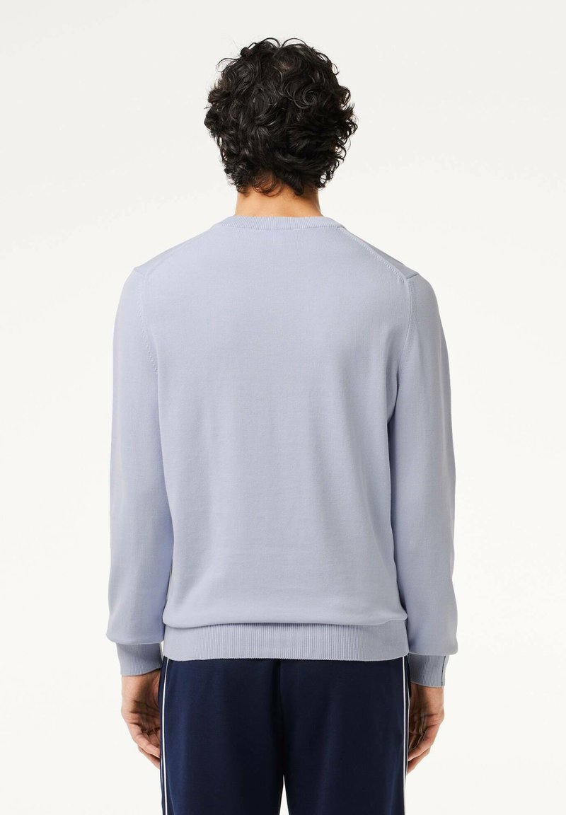 Helles blaues Strickoberteil mit rundem Ausschnitt und gerippten Bündchen, kombiniert mit dunkelblauen Hosen. Glatte Textur, figurbetontes Design und schlichte Optik.