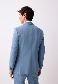 Giacca da uomo azzurro chiaro vista da dietro, con tessuto liscio, spalle strutturate e polsini con bottoni. Design su misura con una sola spacco sul retro.