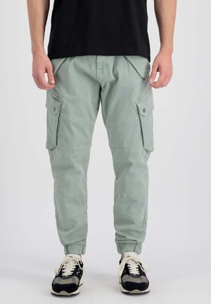 Hellgrüne Cargo-Hosen mit elastischen Bündchen, mehreren Seitentaschen und glatter Textur, getragen mit schwarz-grauen Sneakers.