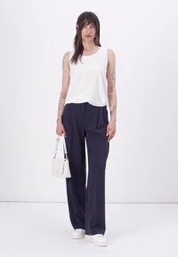 Top sans manches blanc avec un motif œillet associé à un pantalon large bleu marine. Les accessoires incluent un petit sac blanc et des baskets blanches.
