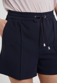 Shorts bleu marine avec une taille élastique, fermeture à cordon et poches latérales. Texture lisse avec une coupe ajustée et sans motifs visibles.
