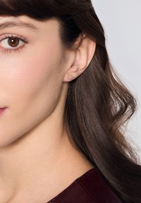 Złote kolczyki z kwiatowym wzorem z małymi akcentami kamieni w układzie gronowym. Gładka tekstura z polerowanym wykończeniem.