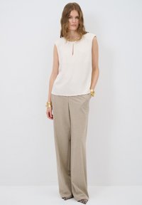 Top sin mangas beige con escote en forma de ojal y cuello embellido, combinado con pantalones de pierna ancha gris claro y zapatos de estampado animal.