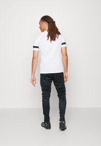 Hvid kortærmet skjorte med sorte stribede detaljer på ærmerne, parret med sorte slim-fit bukser. Glat stof, afslappet atletisk design.