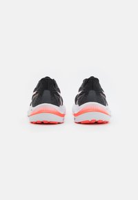 Zapatillas deportivas negras con parte superior texturizada, media suela blanca y suela exterior de color naranja brillante. Presentan un diseño curvado y acentos reflectantes.