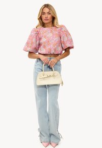 Blouse rose à motif floral avec des manches bouffantes, jean délavé à coupe ample, et un sac à main crème avec des accents dorés et des poignées courtes. Escarpins roses.