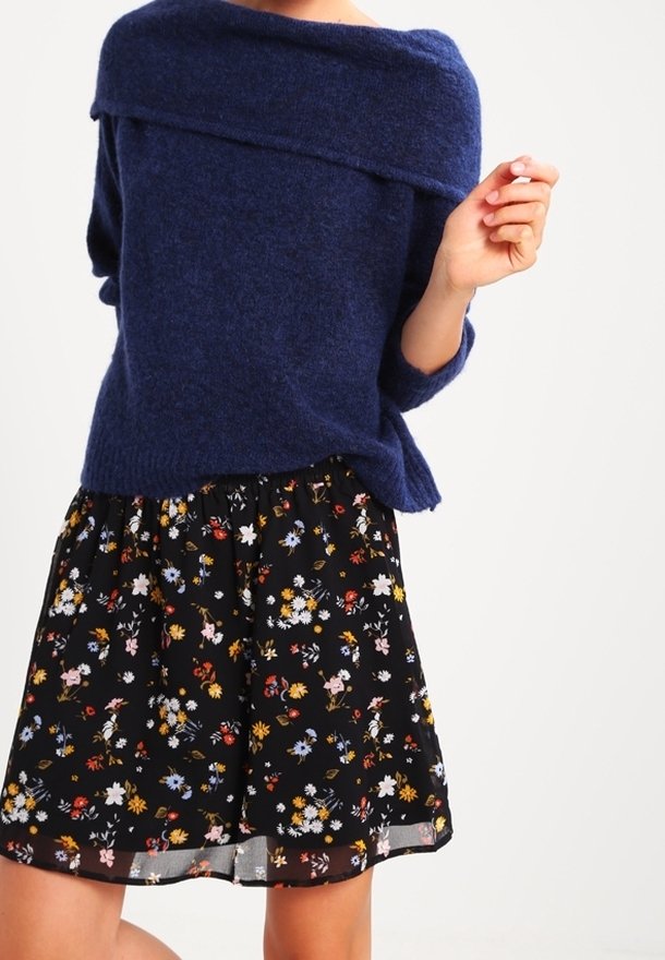 Pull en maille bleu marine avec un design décolleté, associé à une jupe noire à fleurs comportant des fleurs multicolores et un ourlet volanté.