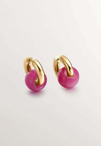 Pendientes de aro en tono dorado que cuentan con una piedra redonda de un vibrante color rosa en el centro, exhibiendo una textura suave y un acabado pulido.