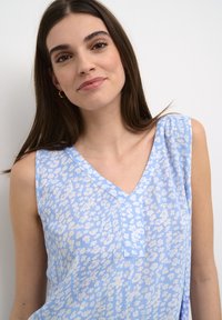 Top sin mangas de color azul claro con escote en V, textura suave y un sutil estampado floral con acentos blancos y dobladillo recto.