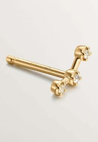 Pieza de joyería en tono dorado que presenta tres piedras transparentes engastadas en garra en una disposición triangular, con un acabado suave y pulido.