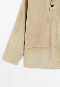 Beige Wildlederjacke mit lockerer Passform, langen Ärmeln und Knopfverschluss. Mit sichtbaren Nähten und einer glatten, weichen Textur.