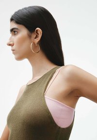 Top de punto verde oliva con escote en u, con una tirante de camiseta rosa visible por debajo. Un gran pendiente de aro dorado realza el look.