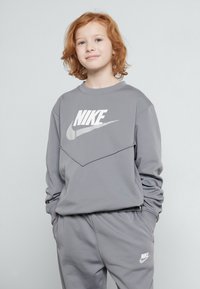 Grå Nike-tröja med en vit logotyp, med en geometrisk design på bröstet, i kombination med matchande grå sweatpants, båda i ett slätt material.