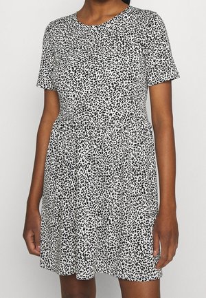 Vrouw draagt een korte mouw, zwart-witte luipaardprintjurk met een geplooide taille en een ronde halslijn.