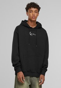 Felpa nera con cappuccio e tasca frontale, con ricamo bianco del logo sul petto. Realizzata in tessuto morbido; vestibilità comoda con polsini a costine.