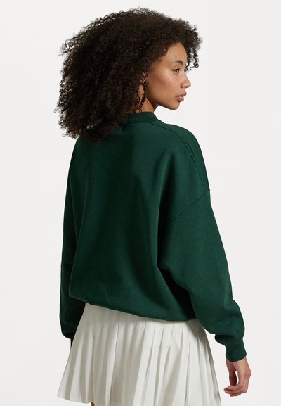 Mørk grønn oversized sweatshirt med rund hals og drop shoulders, kombinert med en plisserte hvit skjørt. Myk stofftekstur, minimalistisk design.