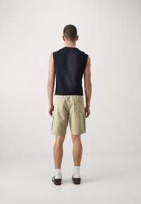 Top senza maniche nero, pantaloni cargo beige con tasche laterali, calzini bianchi e scarpe marroni. Design minimalista con una vestibilità rilassata.