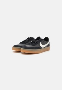 Melni sporta apavi ar zamšas un sintētisku augšdaļu, ar baltu swoosh un gumijas zoli. Šņores ir melnas ar plakanu dizainu.