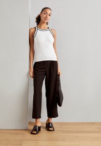 Witte geribbelde tanktop met zwarte biezen, gecombineerd met zwarte wijde broek. Zwarte blokhakken muiltjes en een gestructureerde zwarte handtas maken de look af.